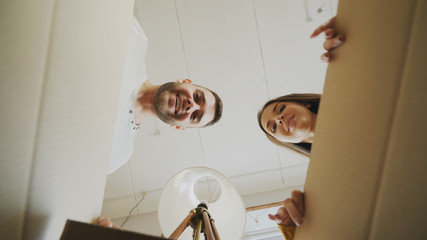 Young happy couple opening cardboard box and looking inside and closing it checking after relocation in new house