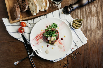 Beef tartare with quail eggs, cornichons and arugula, with bread and a glass of red wine on a dark wooden table