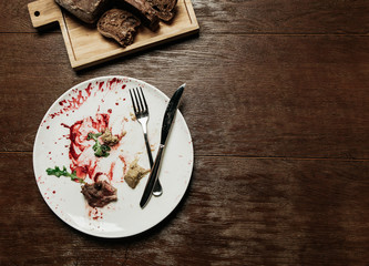 Dirty plate with eaten food,and folded cutlery with a bread board on a wooden table - 187329145