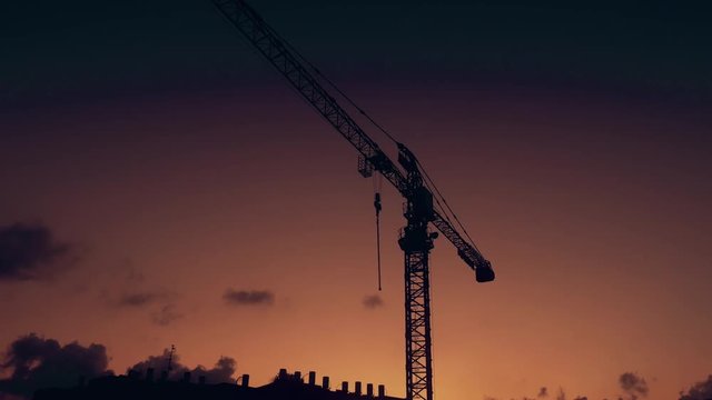 Silhouette of a construction crane at dusk over roof with lot of water heaters. Construction site in Israel.