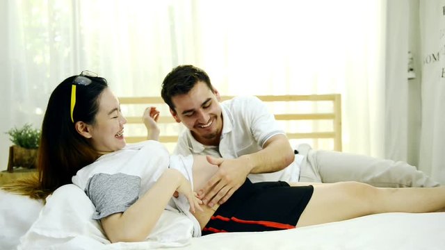 Pregnant woman in bed. Chinese pregnant woman laying in bed relaxing with her white husband. Having fun together.