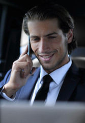 businessman in his car with a laptop talking on the phone