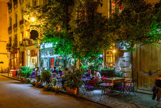 Cozy street with tables of cafe in Paris at night, France