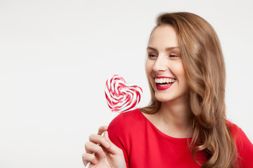 the brunette girl is holding a lollipop as a heart and laughing. For Valentine's Day