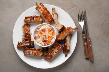 Grilled pork ribs in barbecue sauce and honey with sauerkraut on white plate. Snack to beer on a light stone table, Top view