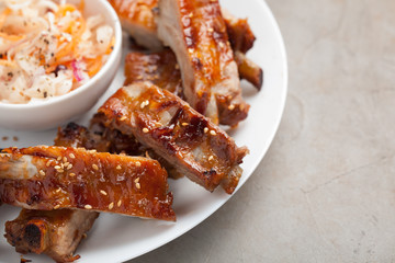 Grilled pork ribs in barbecue sauce and honey with sauerkraut on white plate. Snack to beer on a light stone table, Top view