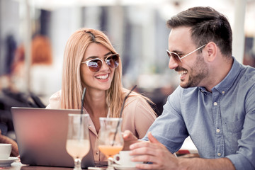 Happy couple in coffee shop using laptop and drink coffee.