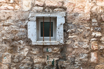 Old stones wall of prison with small window  covered a metal fence