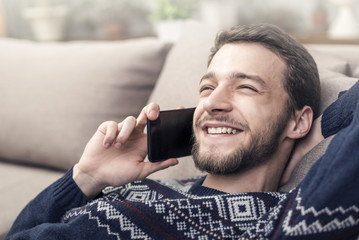 Cheerful young man holding mobile phone and smiling at home.
