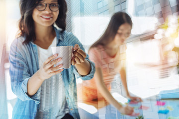 Delicious drink. Selective focus of a cup of tea being held by joyful cheerful delighted woman while being at work