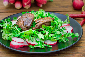 Warm salad with chicken liver, arugula and radish with sauce on the black plate. Wooden rustic background. Selective focus. Top view