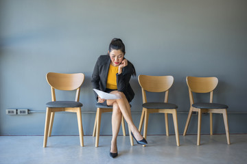 A woman sitting in a chair reading a document while waiting for a job interview in the waiting room.