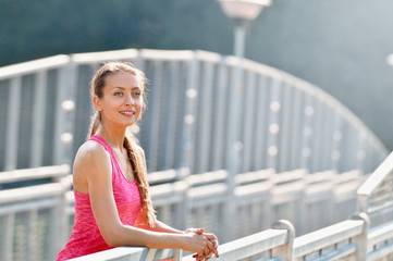 portrait of young woman smiling on urban metal city bridge after running workout