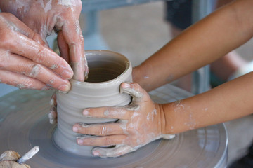 An old hands person and a child making a vase pottery together.