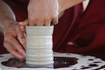 an old hand holding a small hand of a kid to helps and teching how to make a vase pottery together.