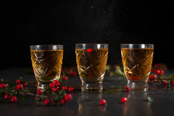 glasses with orange drink and branches with red berries on a dark wet background