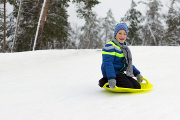 Fototapeta na wymiar Kid flies down a hill on plate for driving on snow