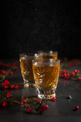 glasses with orange drink and branches with red berries on a dark wet background