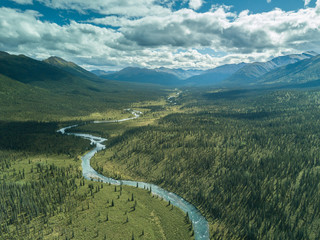 Middle of the day. The sun is high and casts clouds shadows all over the trees in this vast and remote land. An untouched river flows in northern British Columbia with nothing but mountains and trees.