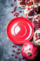Fresh pomegranate, seeds and red empty plate on dark blue stone, concrete background. Top view, space for text.