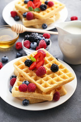 Sweet waffle with berries, milk and honey on grey wooden table