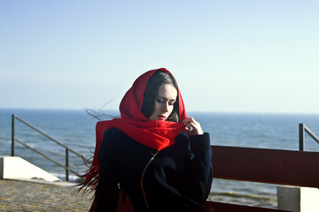 Sad girl in a red kerchief sitting on a seashore bench