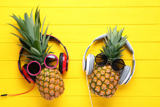 Ripe pineapples with sunglasses and headphones on yellow wooden table