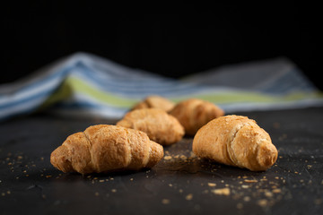 several whole croissants with crumbs and a towel on a dark background