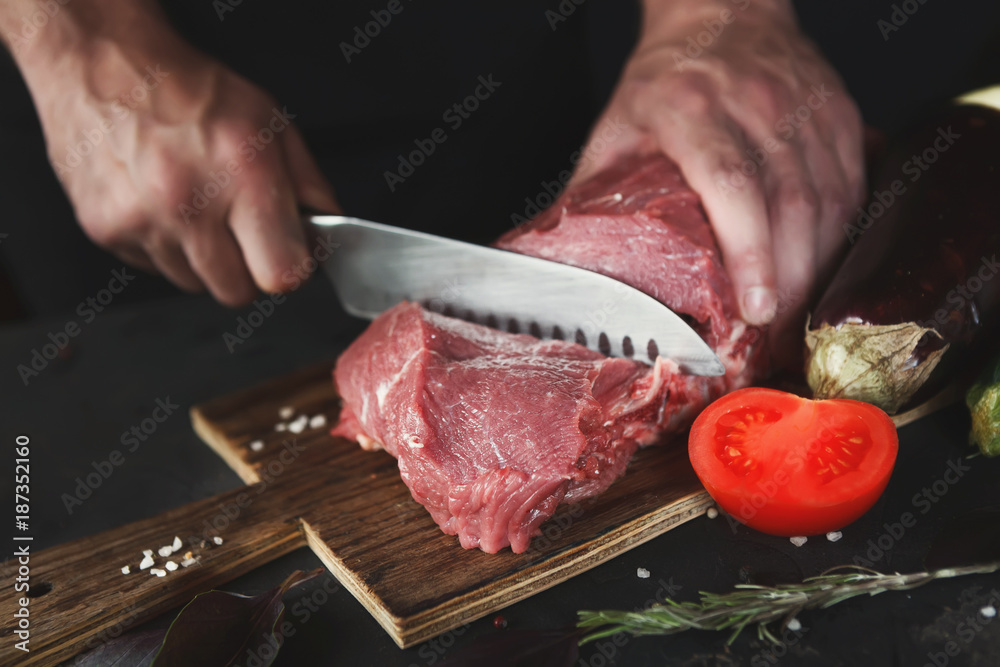 Sticker chef cutting filet mignon on wooden board at restaurant kitchen