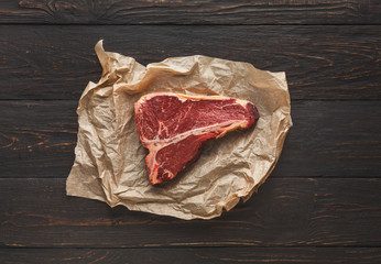 Raw t-bone steak on craft papper on dark background