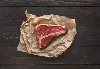 Poster Raw t-bone steak on craft papper on dark background © Prostock-studio