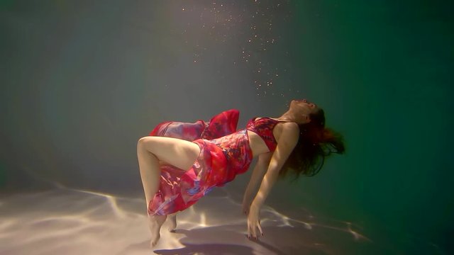 slender girl in a bright dress floats in the weightlessness of water