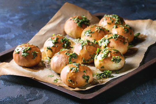 Traditional ukrainian homemade garlic buns pampushki for borscht soup with oil and coriander on old oven tray with baking paper over dark blue texture background. Close up