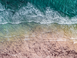 Aerial View of a Vibrant Shoreline. Colourful waves and beach with sun glinting off the surf