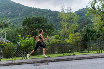 Young fit woman doing cardio exercise, listening to music, running outdoors with green mountain landscape in the background