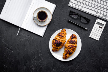 Morning of businessman. Coffee and croissants for breakfast near keyboard and notebook. Black background top view copyspace