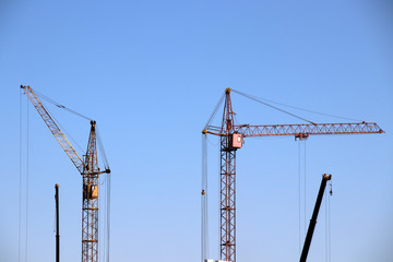 Old tower and telescopic cranes against a blue sky