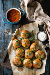 Pan of traditional beetroot borscht soup with sour cream and fresh coriander served with garlic bread buns pampushki, glass vodka, textile linen over dark blue wooden background. Top view, space
