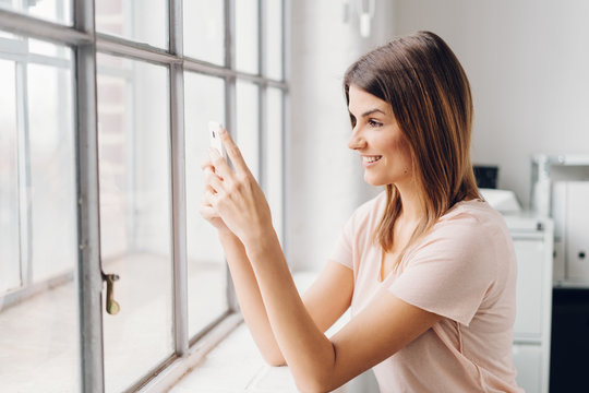 Young smiling woman using mobile phone by window