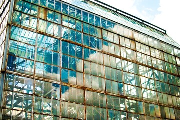 Obraz premium Rusty glass windows of an almost abandoned greenhouse building in botanical garden and reflection of sunlight