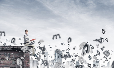 Man on roof edge reading book and symbols flying around