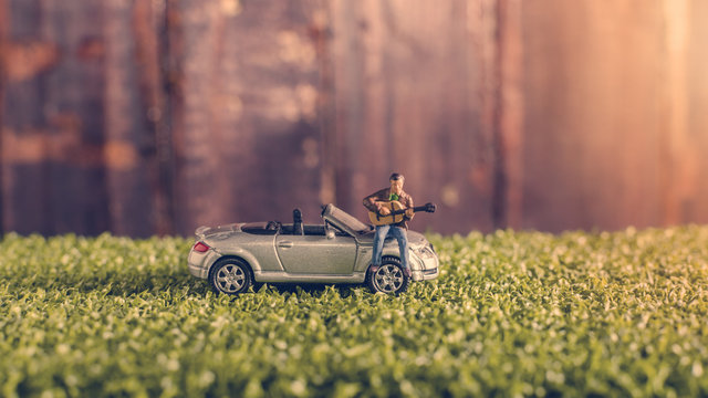 miniature man playing guitar on a car in park