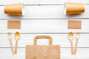 Disposable things. Paper bag, tableware and notebook on white wooden background top view copyspace