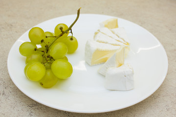 White plate with bunch of green grapes and cheese pieces on stone backgound