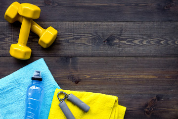 Fitness equipment. Dumbbells, water, expander on dark wooden background top view copyspace