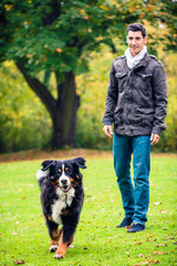 Naklejka na ściany i meble Man walking his dog in autumn park
