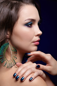 Portrait of beautiful brunette woman on black background and peacock feather earrings