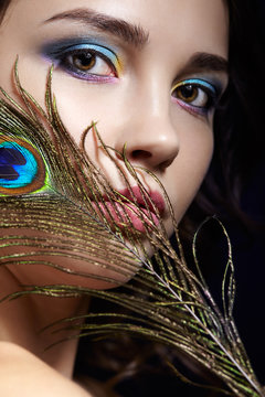 Portrait of beautiful brunette woman on black background and peacock feather