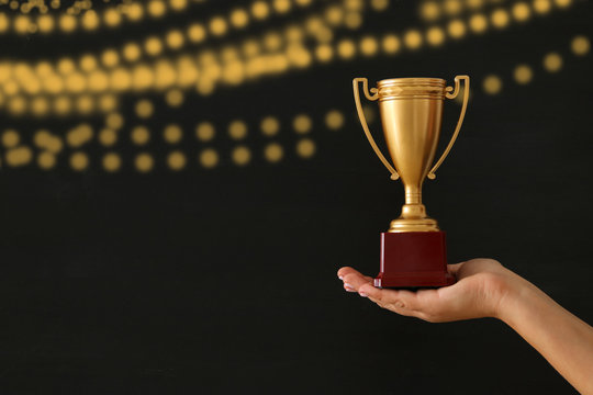 low key image of a woman holding a trophy cup over dark background.