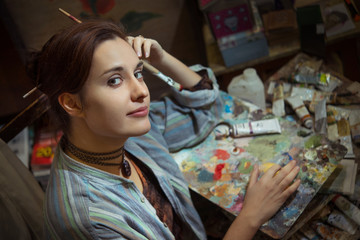 Young woman artist painting with oil paints in the studio workshop